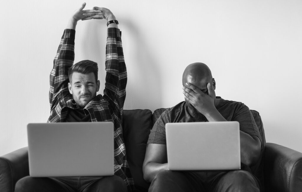 Two men using laptop sitting on sofa